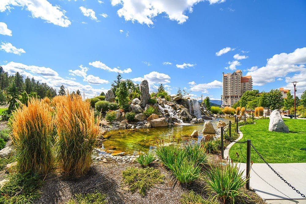 Landscaped waterfall and pond at McEuen Park with the Coeur d'Alene Resort beyond